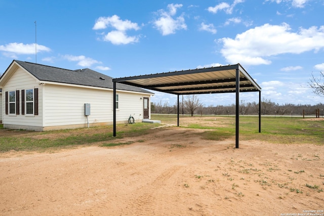 view of side of home with driveway, a shingled roof, and a detached carport