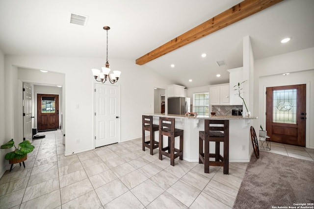 kitchen with visible vents, white cabinets, lofted ceiling with beams, freestanding refrigerator, and a peninsula