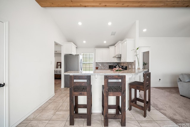 kitchen featuring tasteful backsplash, beamed ceiling, a peninsula, under cabinet range hood, and white cabinetry