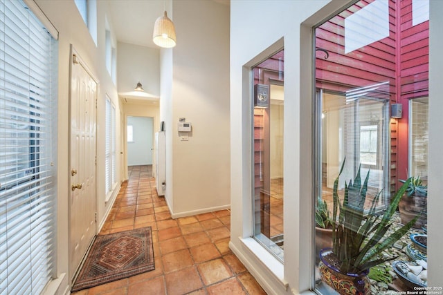 corridor featuring baseboards, a healthy amount of sunlight, and a high ceiling