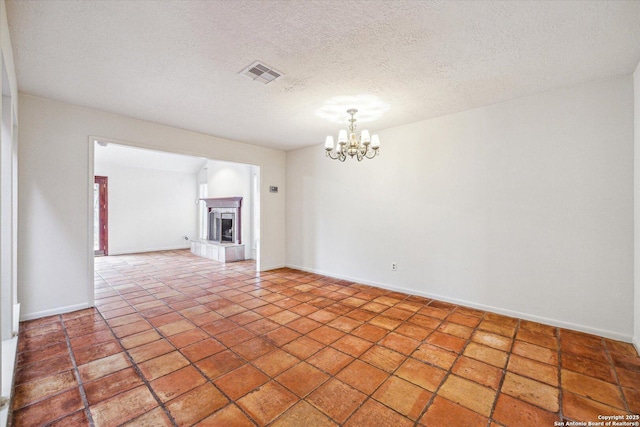 spare room featuring a fireplace with raised hearth, baseboards, visible vents, and an inviting chandelier