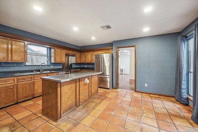 kitchen featuring a center island, brown cabinets, visible vents, a sink, and high end refrigerator