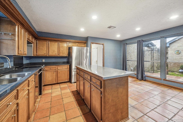 kitchen with a center island, brown cabinets, visible vents, freestanding refrigerator, and a sink