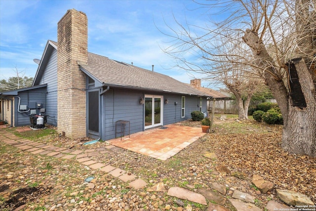 rear view of house with a shingled roof, a chimney, a patio area, and fence