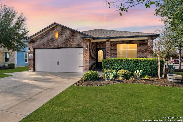 single story home with concrete driveway, a lawn, roof with shingles, an attached garage, and brick siding