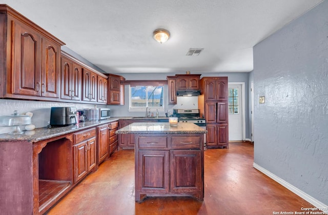 kitchen featuring visible vents, a textured wall, concrete floors, under cabinet range hood, and baseboards