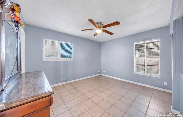 empty room featuring ceiling fan, plenty of natural light, and baseboards