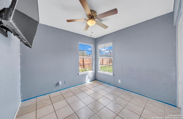 empty room with ceiling fan, a textured wall, and tile patterned floors