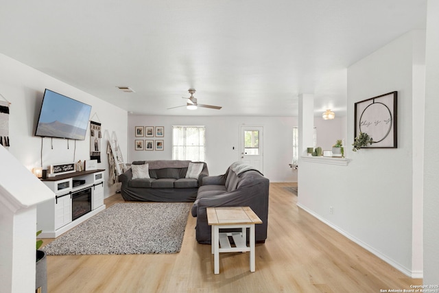 living room featuring a ceiling fan, visible vents, light wood-style flooring, and baseboards