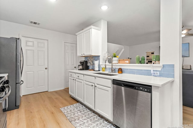 kitchen with tasteful backsplash, visible vents, light wood-style flooring, stainless steel appliances, and a sink