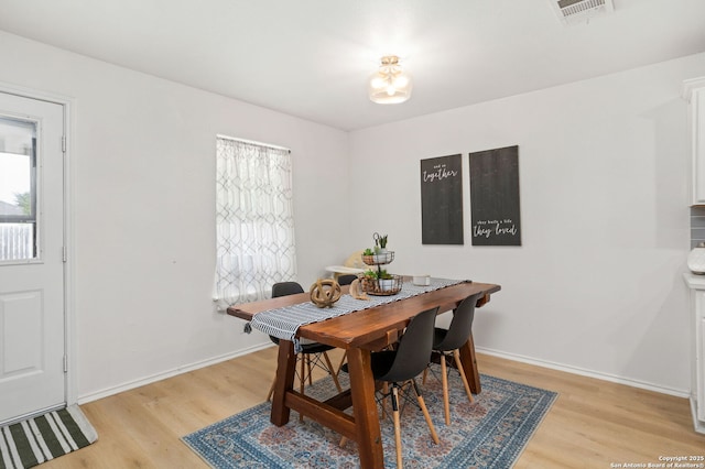 dining space with light wood-type flooring, visible vents, and baseboards