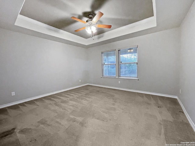 carpeted spare room featuring ceiling fan, baseboards, a raised ceiling, and crown molding