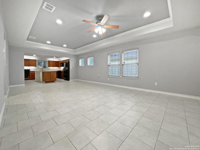 unfurnished living room with a tray ceiling, visible vents, and baseboards