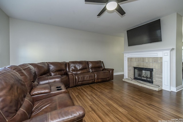 living area featuring baseboards, a tiled fireplace, a ceiling fan, and wood finished floors