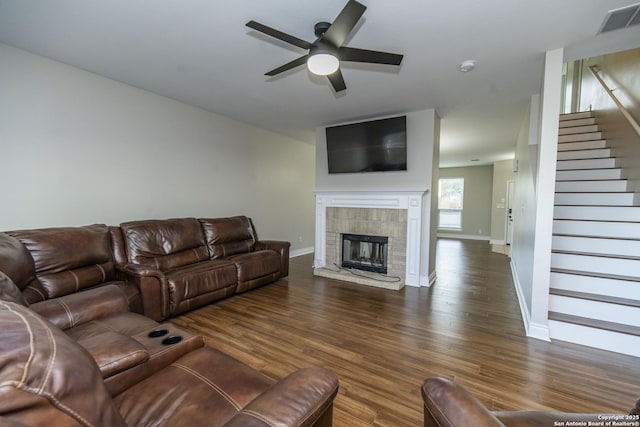 living area with visible vents, a tile fireplace, ceiling fan, wood finished floors, and stairs