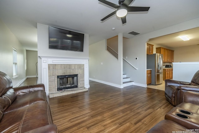 living room with baseboards, visible vents, a tiled fireplace, stairway, and wood finished floors