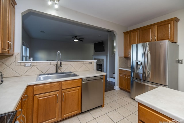 kitchen with brown cabinets, stainless steel appliances, light countertops, a sink, and light tile patterned flooring