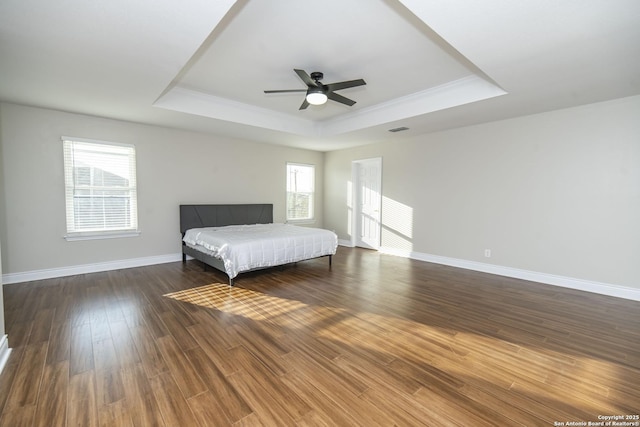 unfurnished bedroom with baseboards, visible vents, ceiling fan, wood finished floors, and a tray ceiling