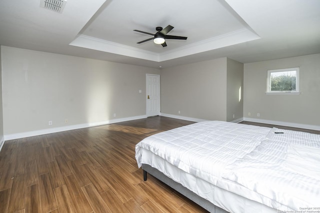 unfurnished bedroom featuring a tray ceiling, visible vents, baseboards, and wood finished floors