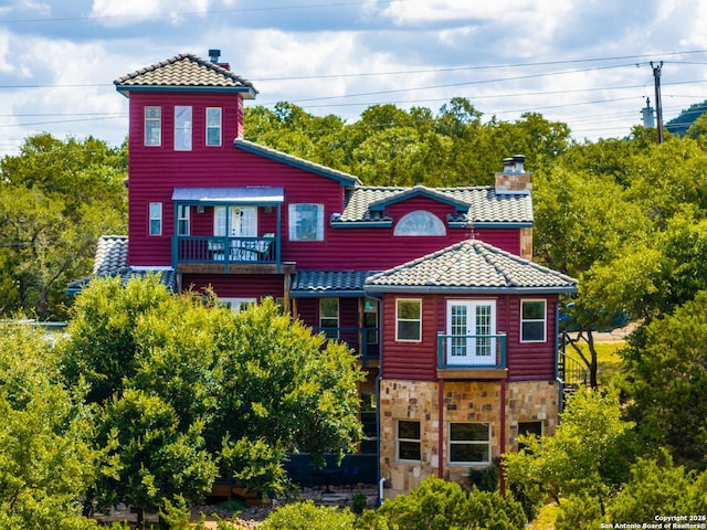 exterior space featuring a balcony, stone siding, a tile roof, and a chimney