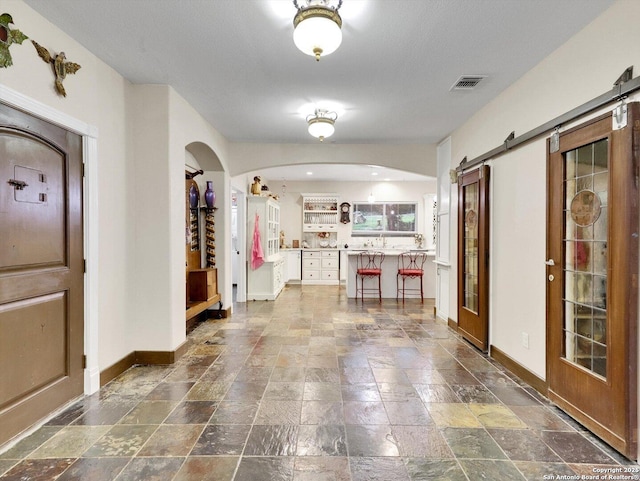 foyer entrance with arched walkways, stone finish floor, visible vents, and baseboards