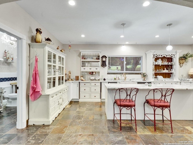 kitchen with recessed lighting, stone finish floor, white cabinetry, and a breakfast bar area