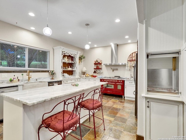 kitchen featuring recessed lighting, a kitchen island, a sink, hanging light fixtures, and wall chimney range hood