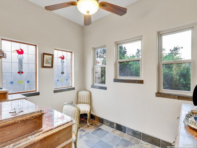 interior space featuring ceiling fan, stone finish flooring, and baseboards