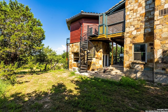 back of property featuring stone siding, log veneer siding, a lawn, and stairs