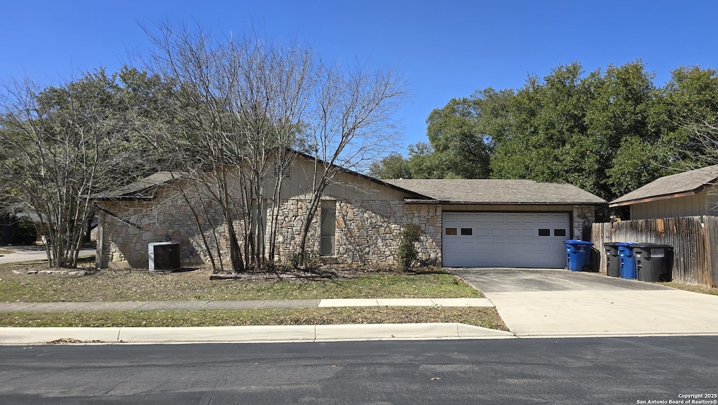 view of front facade with a garage, stone siding, fence, and driveway