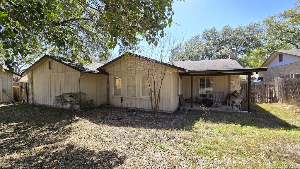 back of property featuring a patio, a chimney, fence, and roof with shingles