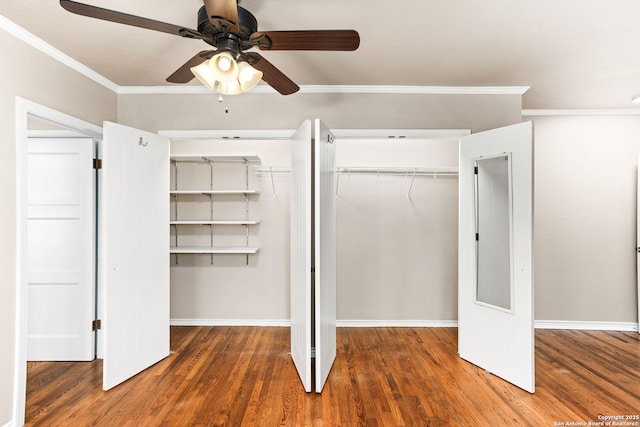 unfurnished bedroom featuring baseboards, a ceiling fan, wood finished floors, crown molding, and two closets