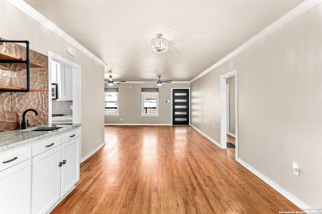 interior space with a ceiling fan, light wood-style flooring, ornamental molding, and baseboards