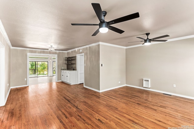 unfurnished living room featuring baseboards, visible vents, ornamental molding, and wood finished floors