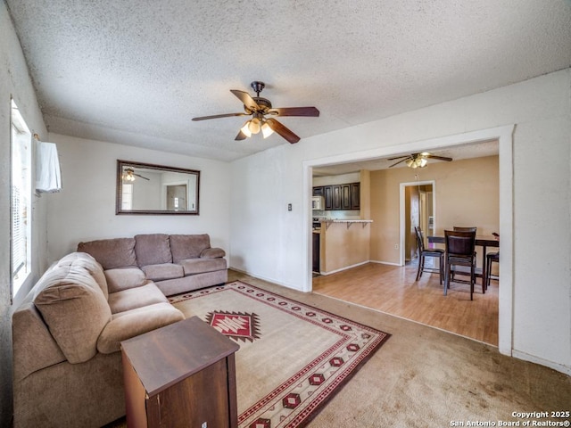 living area featuring ceiling fan, a textured ceiling, and light colored carpet