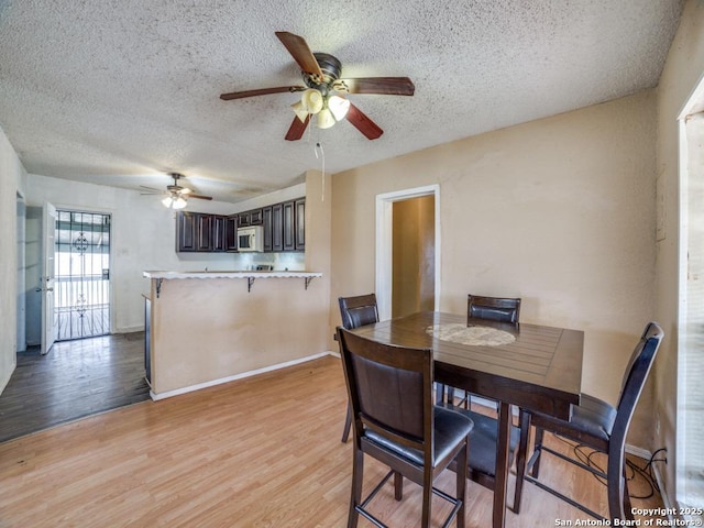 dining area with light wood-type flooring, ceiling fan, a textured ceiling, and baseboards