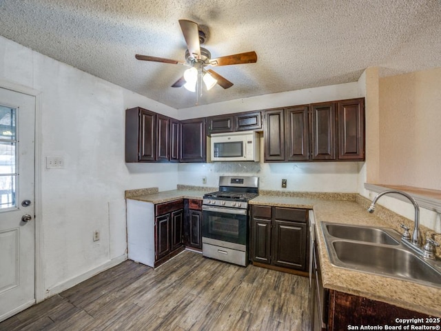 kitchen with dark brown cabinetry, white microwave, dark wood-style flooring, stainless steel range with gas cooktop, and a sink