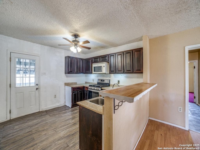 kitchen with a peninsula, white microwave, gas stove, and wood finished floors