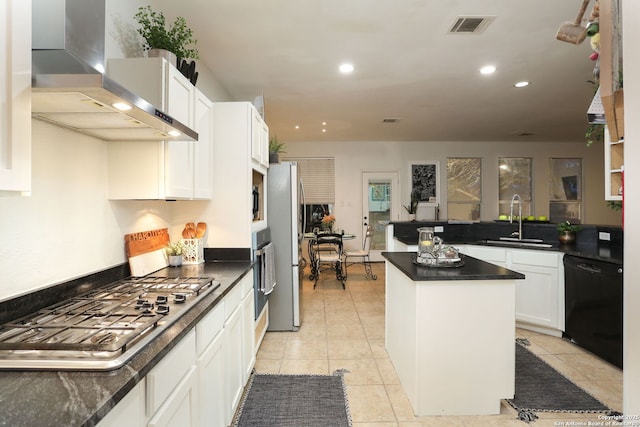 kitchen with white cabinets, dark countertops, wall chimney exhaust hood, stainless steel appliances, and a sink