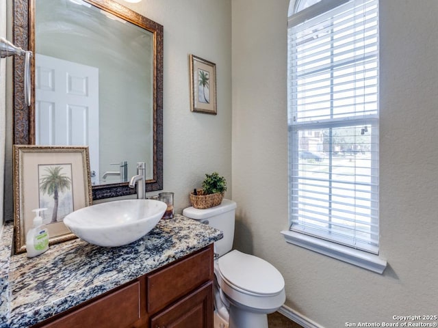 half bath featuring a wealth of natural light, toilet, vanity, and a textured wall