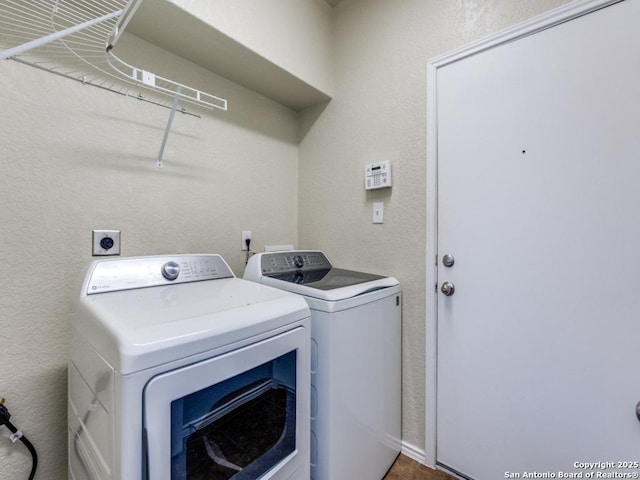 washroom with laundry area, a textured wall, and washer and clothes dryer