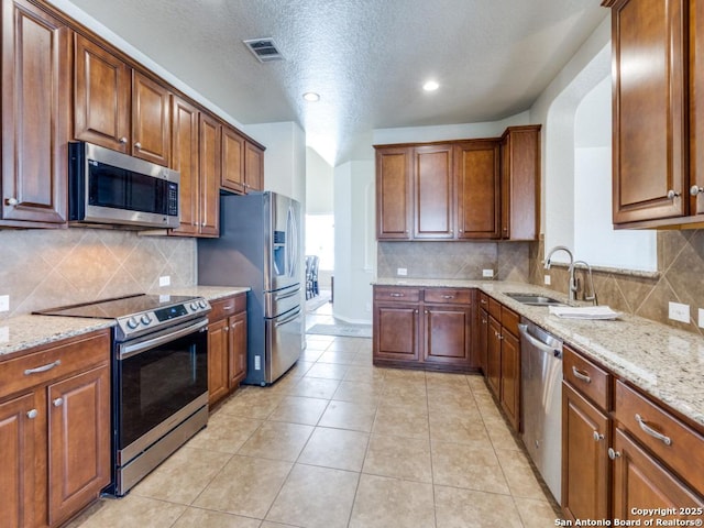 kitchen featuring visible vents, light stone countertops, appliances with stainless steel finishes, light tile patterned flooring, and a sink