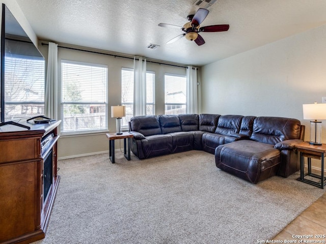 living area featuring visible vents, baseboards, ceiling fan, light tile patterned flooring, and a textured ceiling