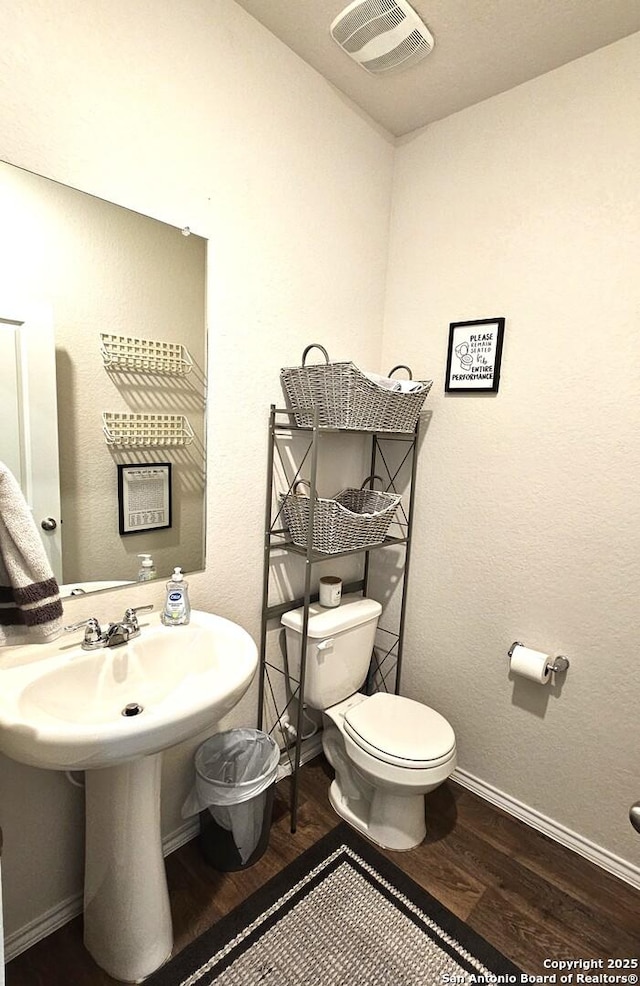 half bathroom with toilet, wood finished floors, visible vents, and baseboards