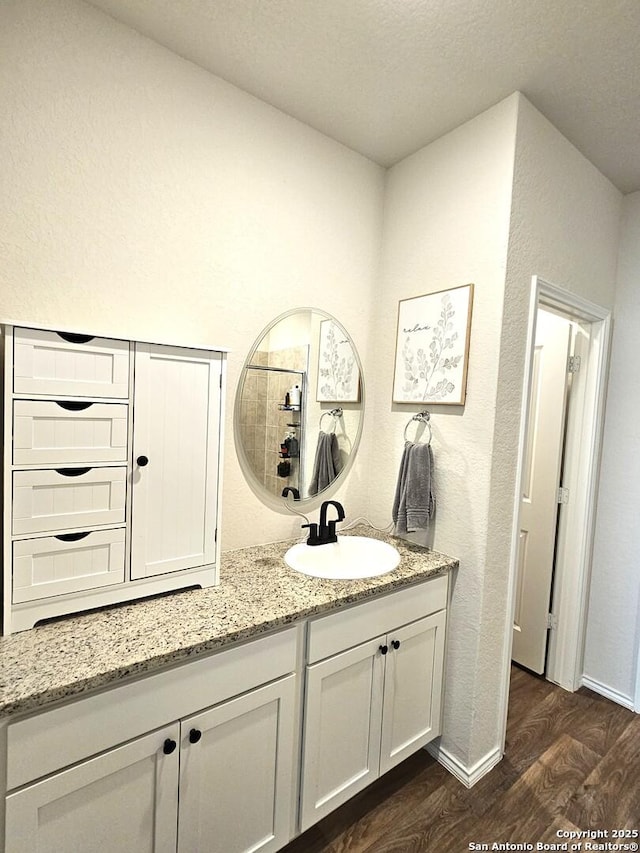 bathroom featuring a textured wall, baseboards, wood finished floors, and vanity