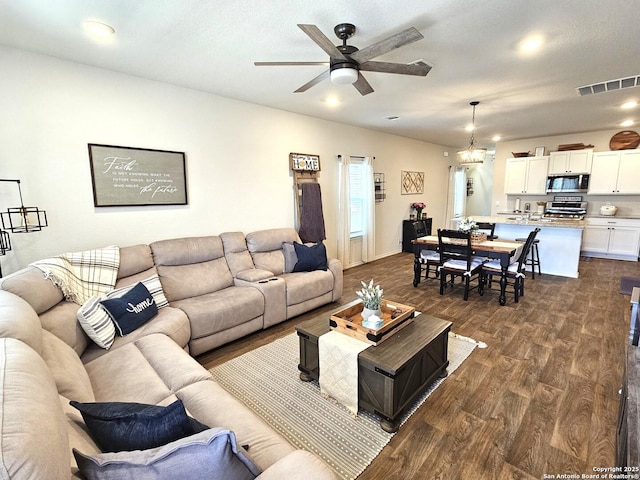 living room featuring dark wood-style floors, visible vents, and ceiling fan with notable chandelier