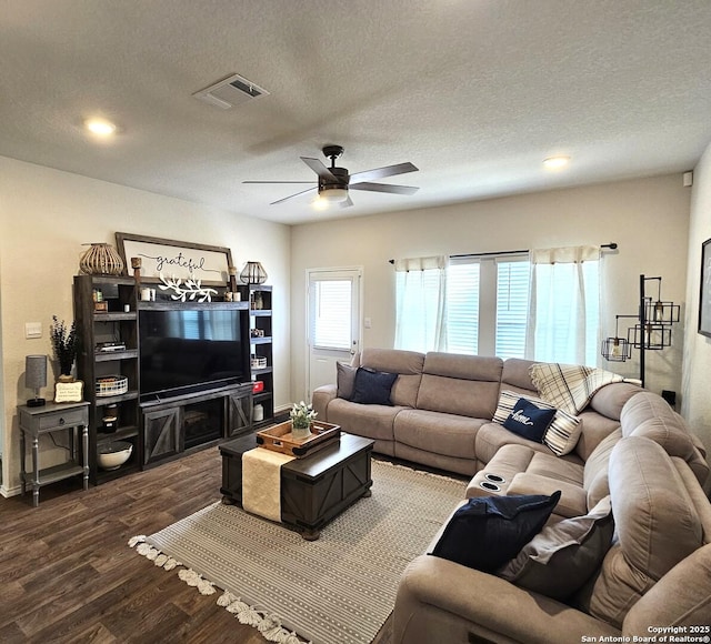 living area featuring dark wood-style floors, ceiling fan, visible vents, and a textured ceiling