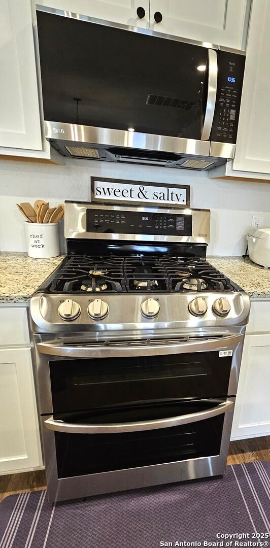 kitchen with stainless steel appliances, white cabinets, and light stone countertops