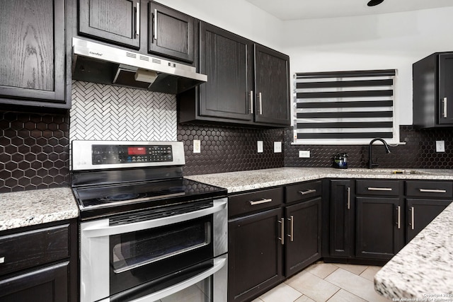 kitchen with light tile patterned floors, tasteful backsplash, under cabinet range hood, double oven range, and a sink