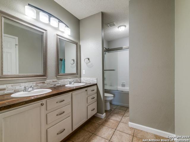 full bath with double vanity, a textured ceiling, toilet, and a sink